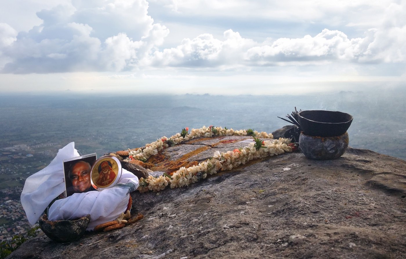The consecrated lingam at the summit of Arunachala, garlanded with flowers, a photograph of Guru Sri Subramanium resting beside it, the plain of Tamil Nadu far below